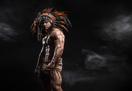 American Indian Apache warrior chief  in traditional clothing and feathered headdress with weapon. Indian chieftain of the tribe with muscled strength body with arrows.