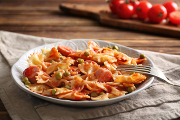 Plate with delicious pasta and sausage on wooden table