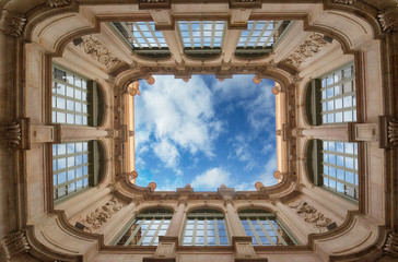 Bottom wide angle view of historic inner courtyard with beautiful facade building complex with blue sky and clouds and reflection in windows in Barcelona, Spain. Geometric shape