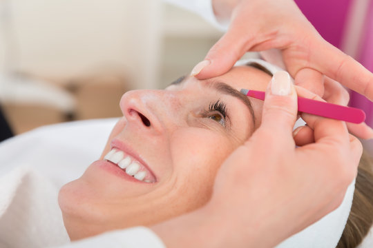 Smiling beautiful woman gets eyebrow correction procedure in salon
