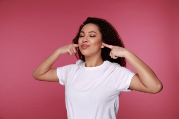 Beautiful young vietnamese woman covering her ears with palms over pink background