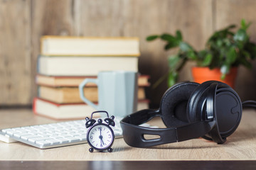Alarm clock, headphones and keyboard on the office desk with books. Office concept, work day,...