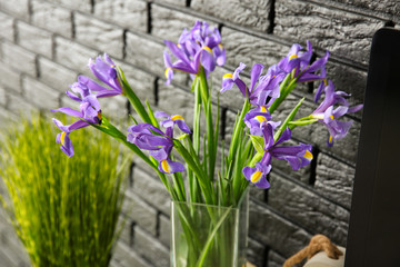 Vase with beautiful flowers near dark brick wall