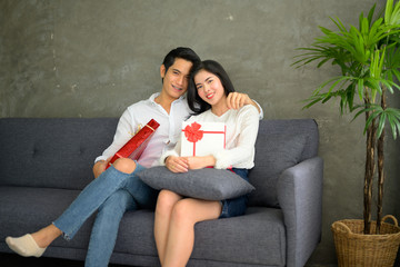 Obraz premium Beautiful young couple at home. Hugging, kissing and enjoying spending time together while celebrating Saint Valentine's Day with gift box in hand