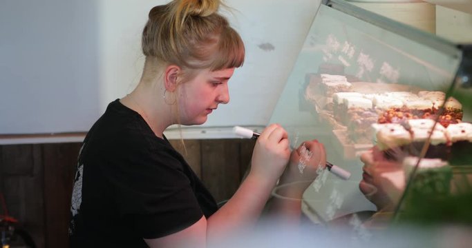 Woman Writing the Prices of Cakes on the Glass