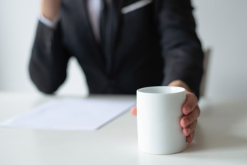 Closeup of business man drinking coffee at workplace. Entrepreneur wearing suit and working at desk. Office occupation and workplace concept. Cropped front view.
