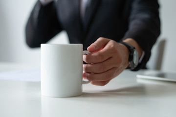 Closeup of business man drinking tea at workplace. Entrepreneur wearing suit and working at desk....