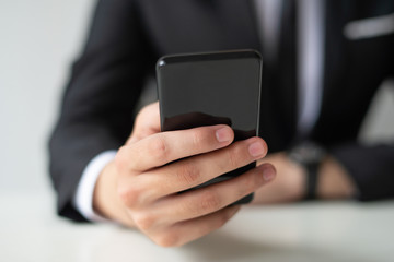 Closeup of business man holding and using smartphone. Person texting on digital gadget. Business and communication concept. Cropped front view.