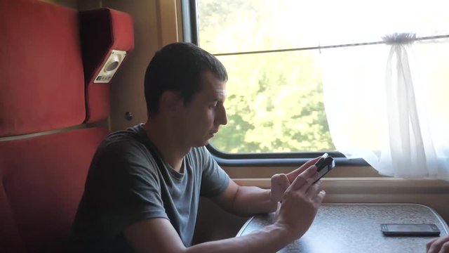 Profile portrait of young positive man traveler and smiling through the pictures via social media. slow motion lifestyle video . uploading photo using cell phone while riding home by train wagon
