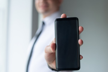 Closeup of entrepreneur showing empty smartphone screen. Business man holding digital device. Technology and promotion concept. Cropped front view.
