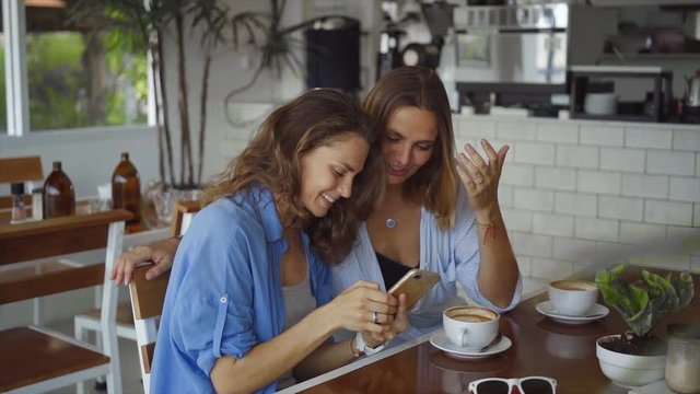 Two woman sharing coffee using smartphone in cafe in slow motion
