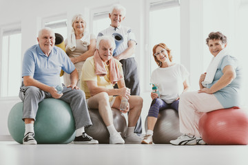Group of active seniors sitting on exercising balls in modern fitness center after sport's training - obrazy, fototapety, plakaty