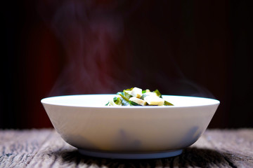 Hot food with hot steam in a white bowl on a wooden table