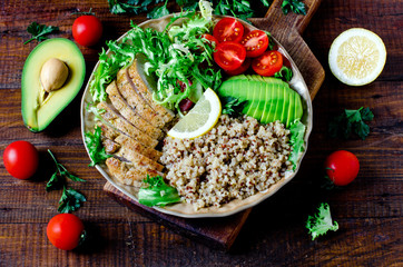 Healthy salad bowl with quinoa, tomatoes, chicken, avocado, lime and mixed greens, lettuce, parsley on wooden background close up. Food and health.