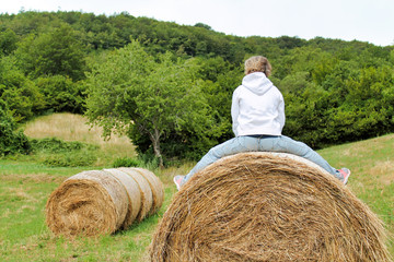Naklejka na ściany i meble girl playing sitting on a bale of hay in a meadow