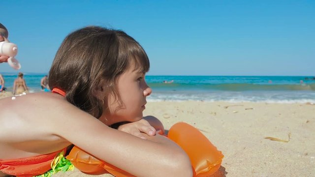 Woman spread sunblock on the childs body. A mother smears sunscreen on her daughter's back.