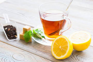Black tea ceremony - glass full of tea, sugar, yellow lemon, tea leaves, spices on a wooden boards background