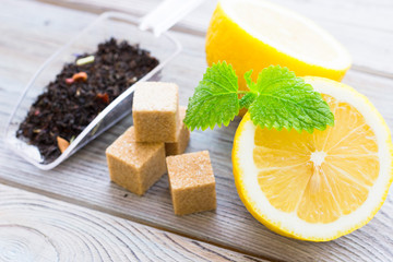 Black tea ceremony - glass full of tea, sugar, yellow lemon, tea leaves, spices on a wooden boards background