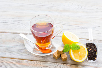 Black tea ceremony - glass full of tea, sugar, yellow lemon, tea leaves, spices on a wooden boards background