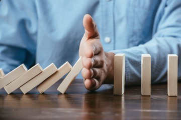 close up view of man sitting at desk and preventing wooden blocks from falling