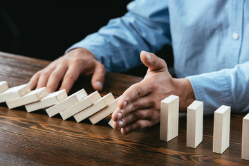 Obraz premium partial view of man sitting at desk and preventing wooden blocks from falling