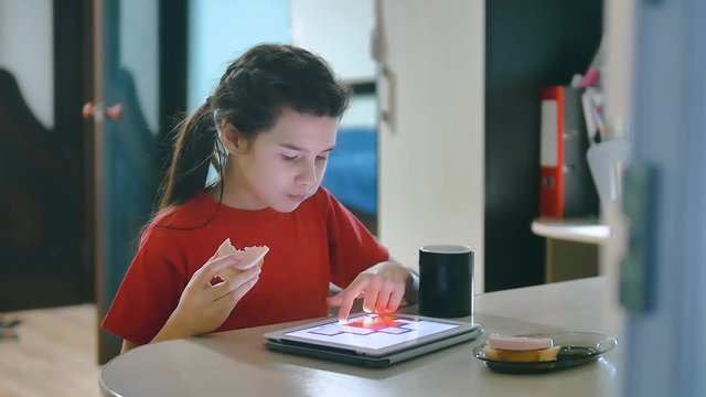 little girl playing digital tablet eating sandwiches. little girl sitting at the table playing digital tablet has a snack in online games sandwiches social lifestyle media. girl and tablet concept