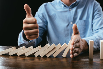 partial view of man sitting at desk, showing thumb up sign and preventing wooden blocks from falling