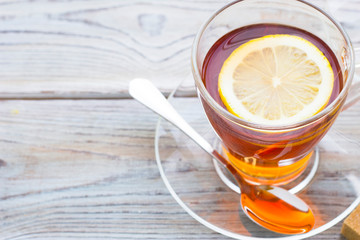 Black tea ceremony - glass full of tea, sugar, yellow lemon, tea leaves, spices on a wooden boards background