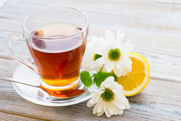 Black tea ceremony - glass full of tea, sugar, yellow lemon, tea leaves, spices on a wooden boards background