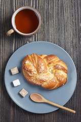 Plate with tasty bun and cup of tea