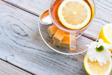 Black tea ceremony - glass full of tea, sugar, yellow lemon, tea leaves, spices on a wooden boards background