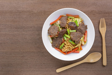 top view of hot and spicy stir fried instant noodle with beef and vegetable in a ceramic plate on wooden table. asian homemade style food concept.