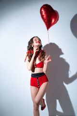 Girl in a red swimsuit, with a ball in the form of a heart near the wall