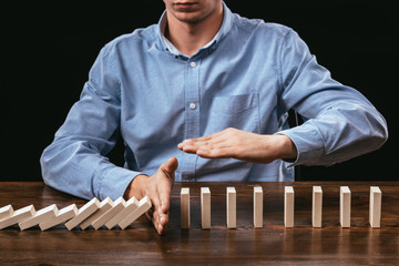cropped view of man preventing wooden blocks from falling isolated on black