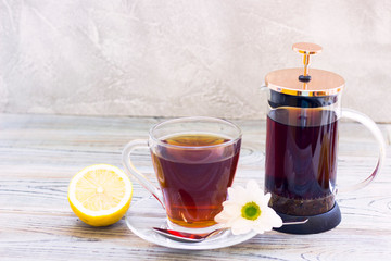 Black tea ceremony - glass full of tea, glass pot, sugar, yellow lemon, tea leaves, spices on a wooden boards background