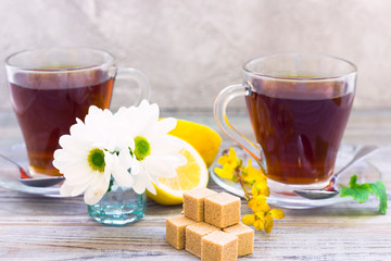 Black tea ceremony - glass full of tea, glass pot, sugar, yellow lemon, flower, tea leaves, spices on a wooden boards background