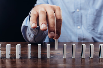 partial view of man picking domino from row on desk isolated on black