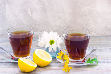 Black tea ceremony - glass full of tea, glass pot, sugar, yellow lemon, flower, tea leaves, spices on a wooden boards background
