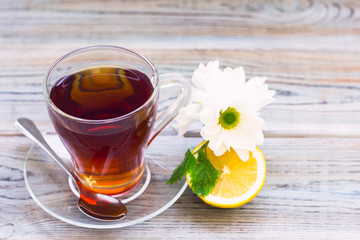 Black tea ceremony - glass full of tea, glass pot, sugar, yellow lemon, flower, tea leaves, spices on a wooden boards background