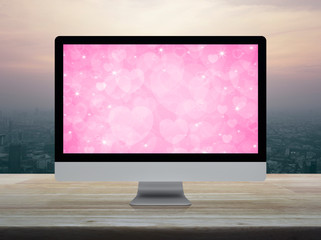 Desktop modern computer monitor with pink love heart screen on wooden table over modern city tower and skyscraper at sunset sky, vintage style, Business internet dating online, Valentines day concept