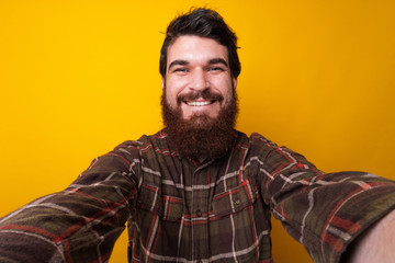 Fototapeta premium Portrait of smiling bearded man taking selfie over yellow background