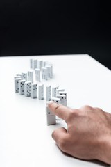 cropped view of man pointing at domino row on white table isolated on black