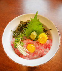 Japanese traditional cuisine minced raw tuna belly on rice bowl (maguro don) with egg yolk, bean sprouts, wasabi, perilla leaf (shiso), shreded dried seaweed and  chrysanthemum flower (kiku)