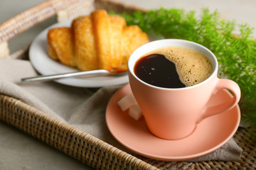 Cup of hot coffee and plate with croissant on tray