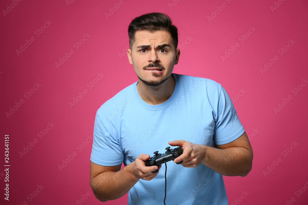Wall mural Emotional young man playing video game on color background - Wall murals