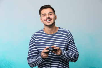 Happy young man playing video game on color background