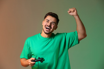 Happy young man after winning video game on color background