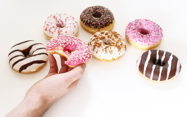 Close up of a man holding in his hands a pink donut with sprinkles on a wooden table. Concept of breakfast. Food detail. Close up. Pastel color.