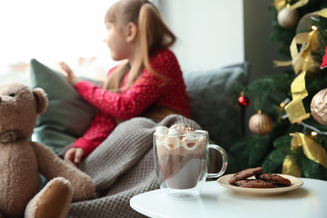 Cup of hot chocolate and tasty cookies on table in room of cute little girl