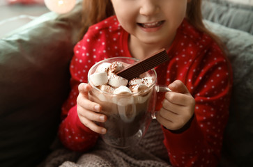 Cute little girl drinking hot chocolate near window